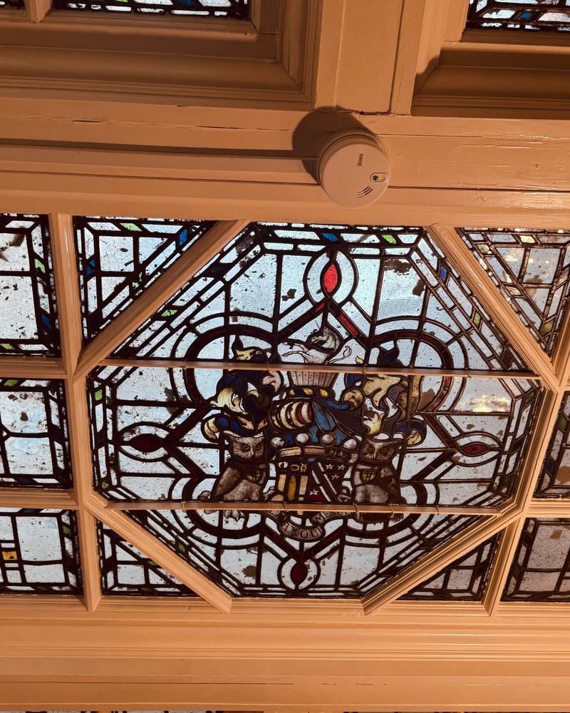 Looking up at a timber-framed laylight with heraldic stained glass panels.