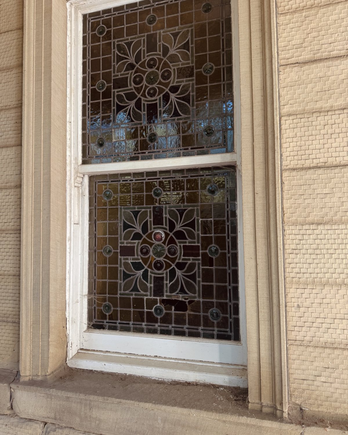 A stone-framed sash window with leaded stained glass in both panes.