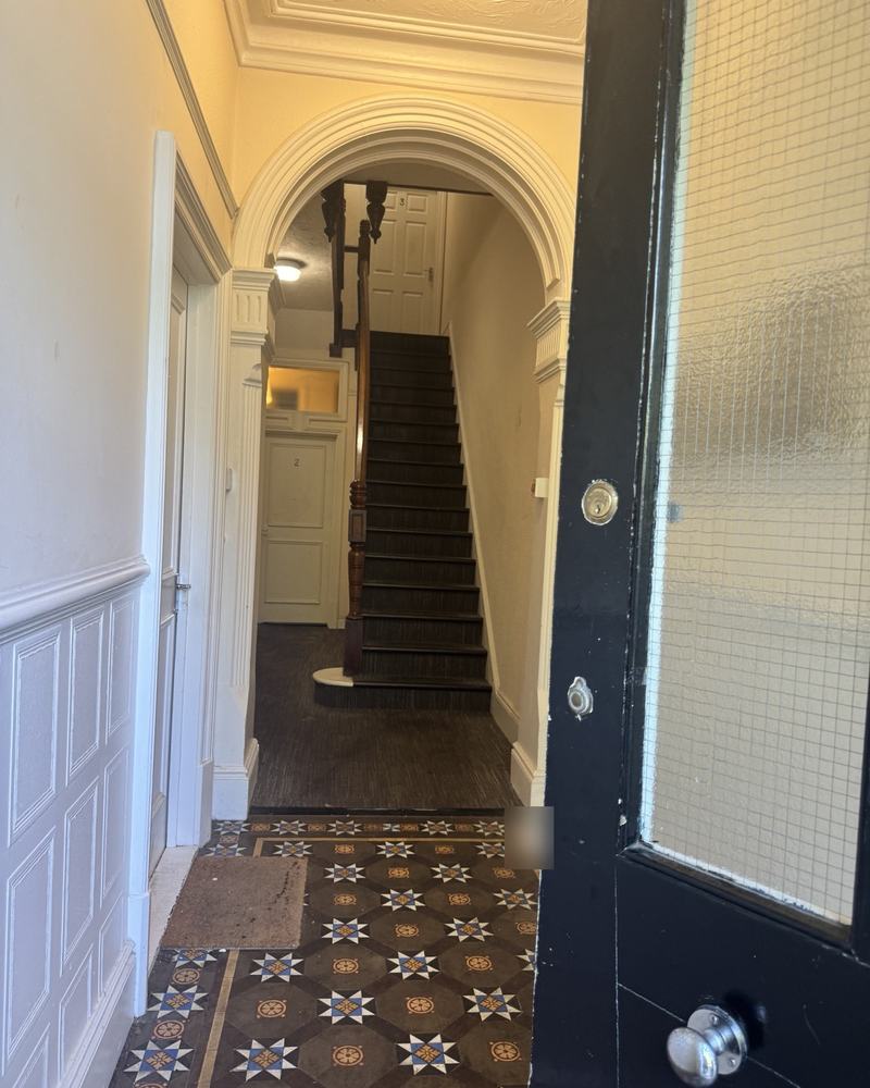 A Victorian entrance hall with a patterned tiled floor, an arch and stairs beyond.