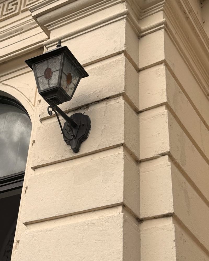 A lantern on a cream stucco porch, with a Greek key frieze above an arched window.