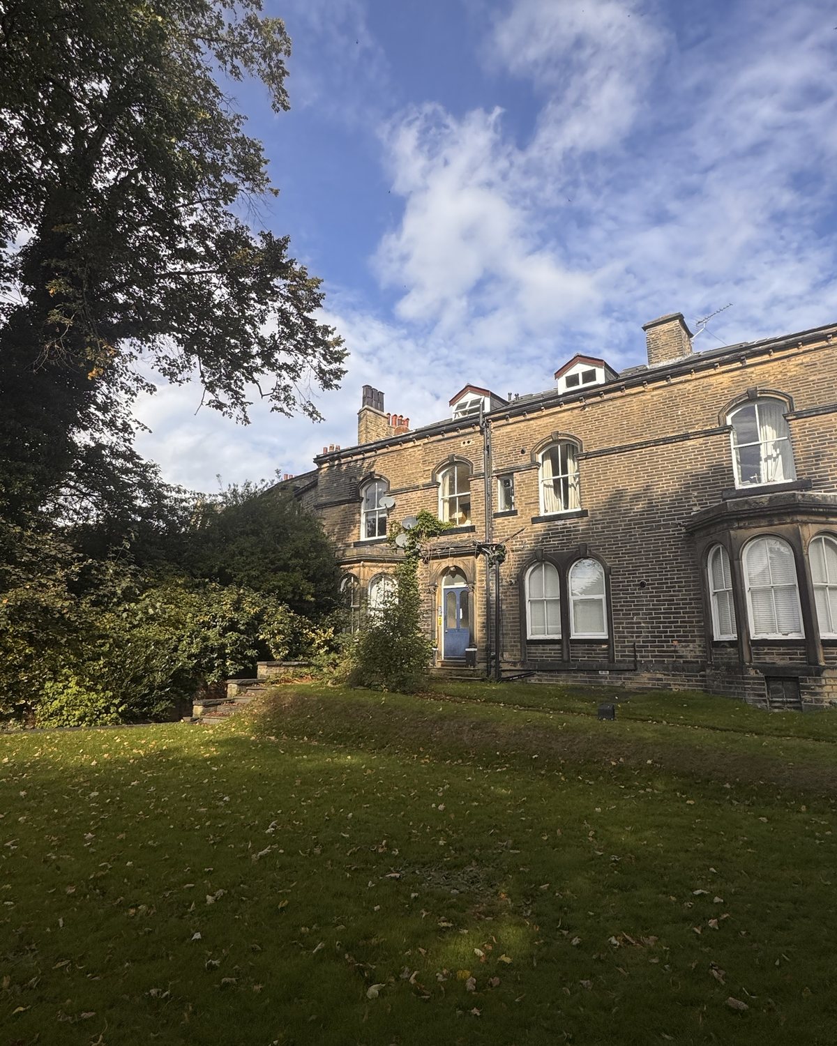 A large stone house with bay windows and a blue front door, across a lawn.