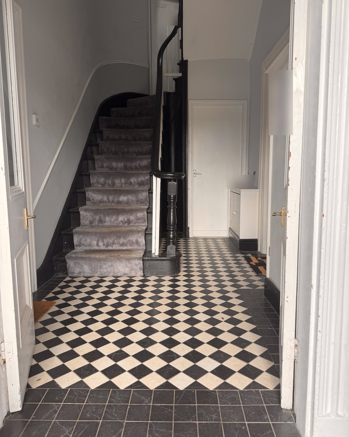 A hallway with a black and white chequered tiled floor and a staircase with a curled black handrail.