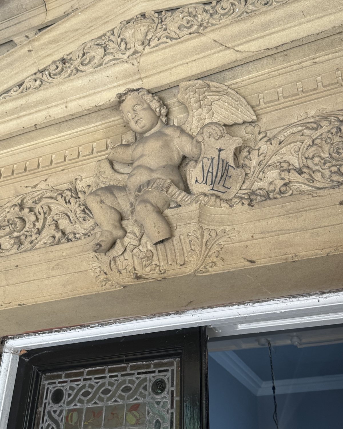 A carved stone cherub above a front door, holding a shield.