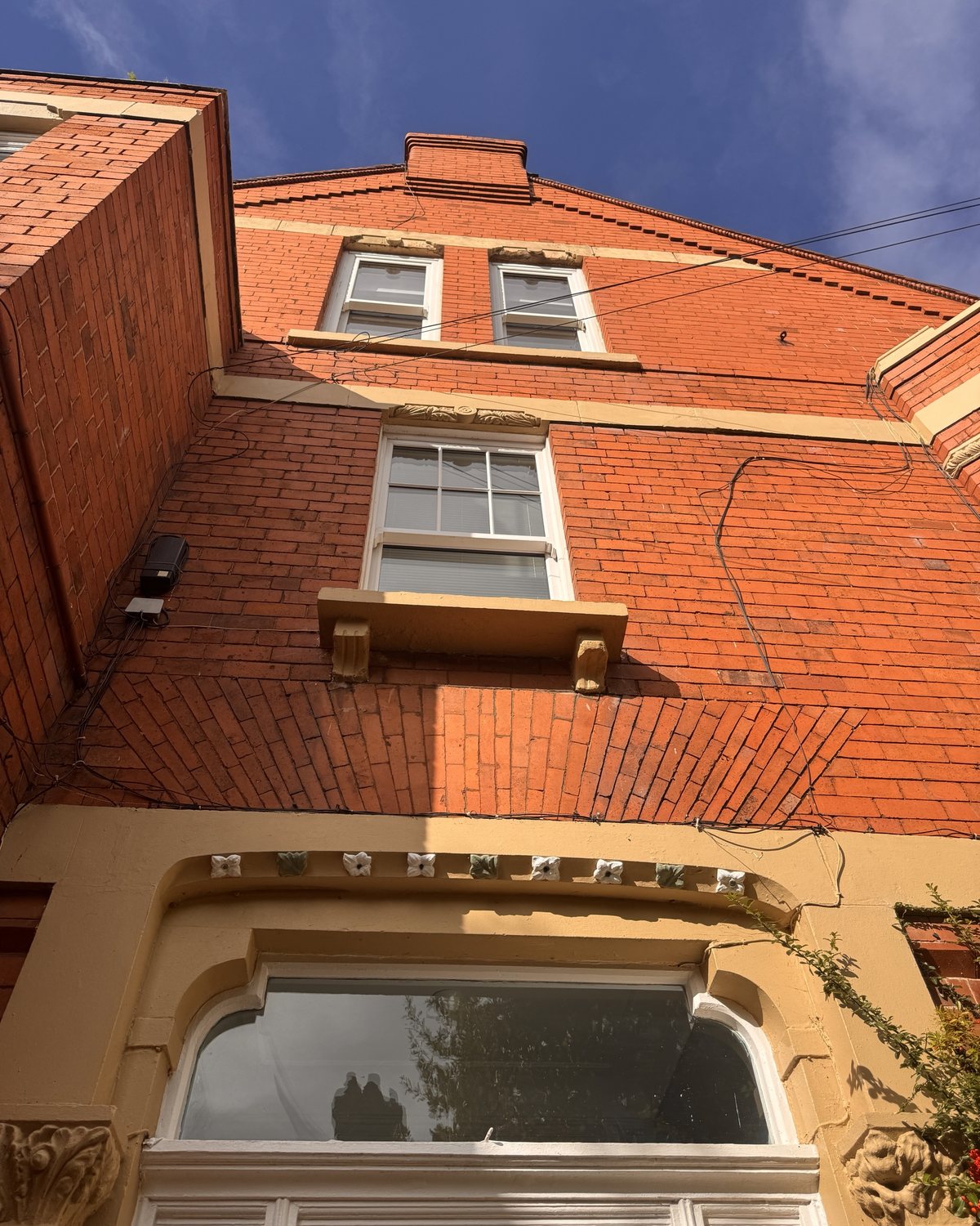 Looking up a red-brick gable, with a row of small glazed flowers over the ground-floor window.