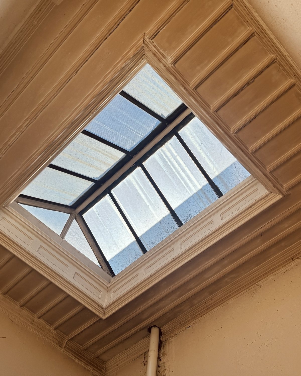 Looking up at a glazed lantern skylight set in a panelled ceiling.